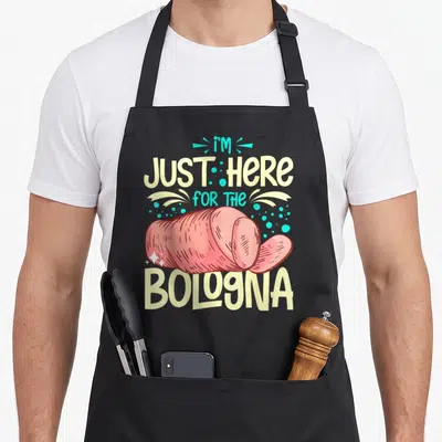 Bologna meat aprons - Pink cartoon bologna log slice with pale yellow and turquoise text and scattered dots — shown on a black cotton canvas apron against a white background