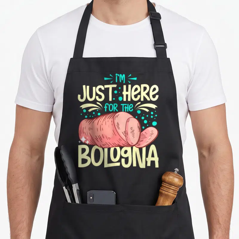 Bologna meat aprons - Pink cartoon bologna log slice with pale yellow and turquoise text and scattered dots — shown on a black cotton canvas apron against a white background