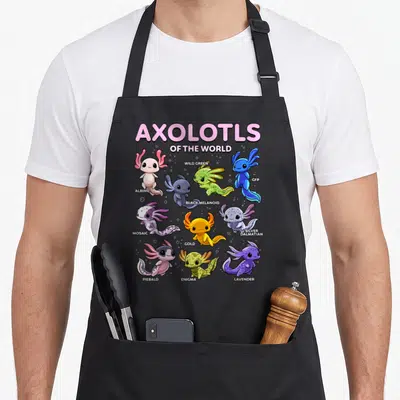 Axolotl kawaii apron - Nine cartoon axolotls in pink, green, blue, purple, and gold with variety labels — shown on a black cotton canvas apron against a white background