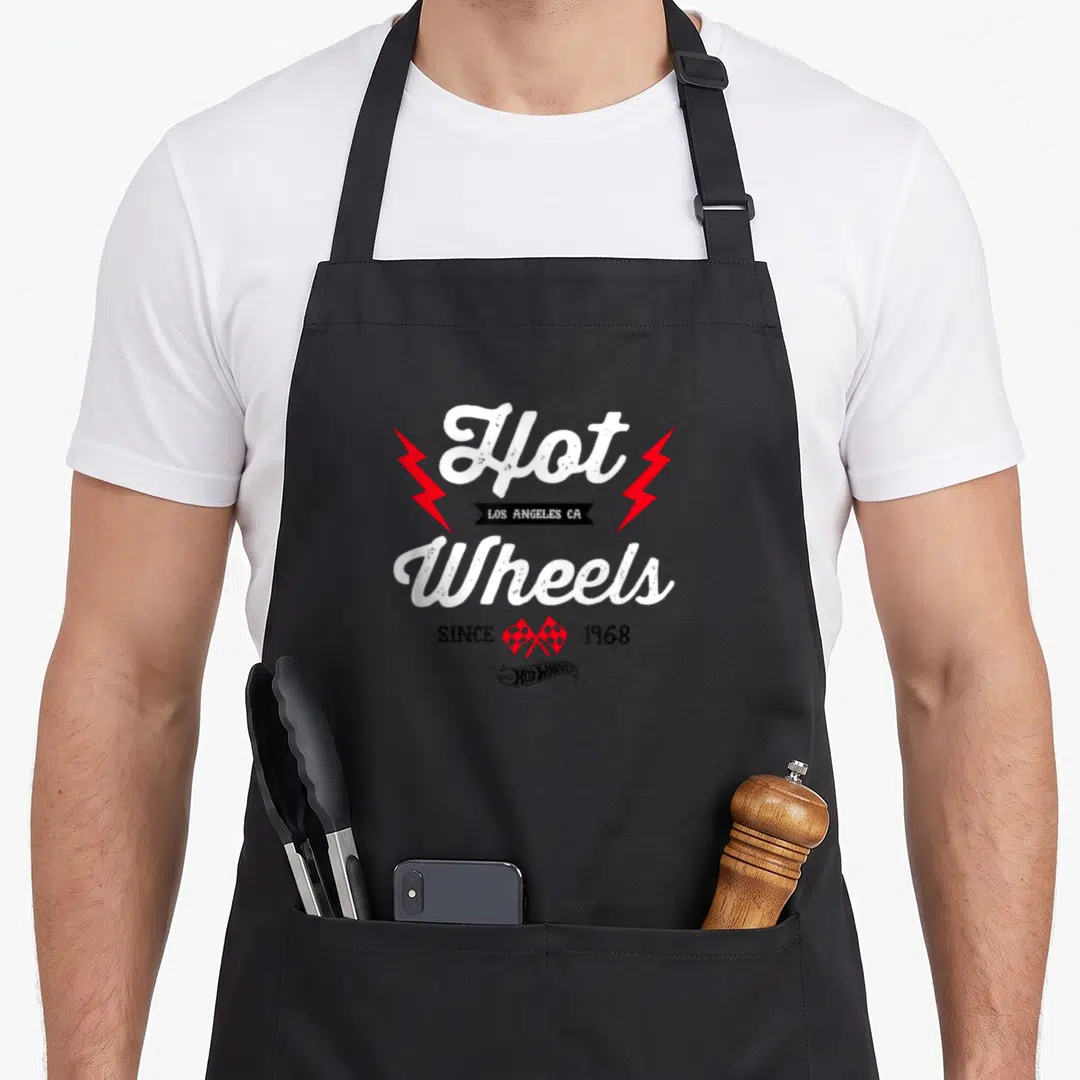Emblem wheel apron - Stacked white Hot Wheels text flanked by red lightning bolts and checkered flags with black banner — shown on a black cotton canvas apron against a white background