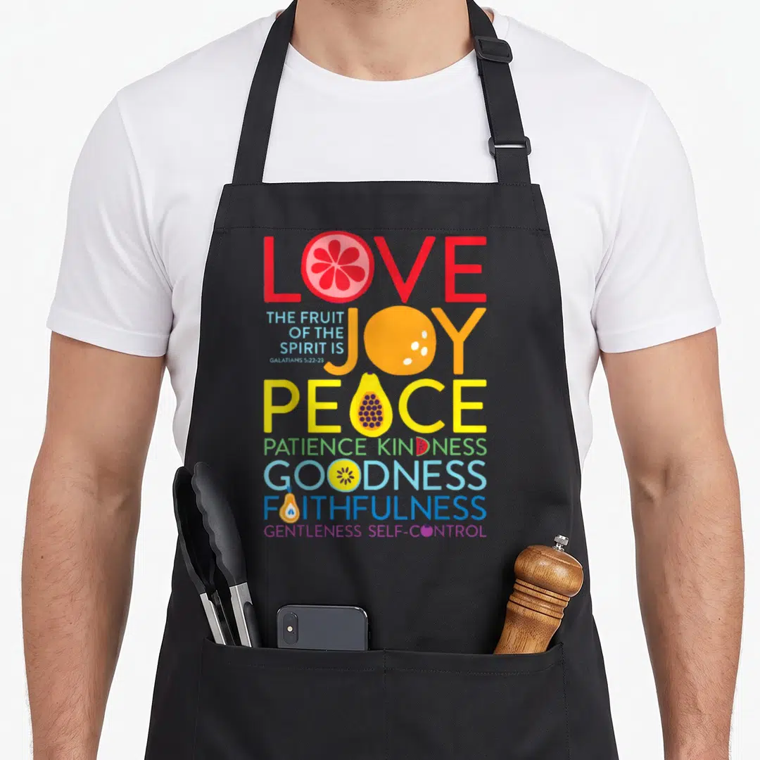 Galatian fruit apron - Stacked colorful text of Galatians 5:22-23 with fruit illustrations replacing letters in red — shown on a black cotton canvas apron against a white background