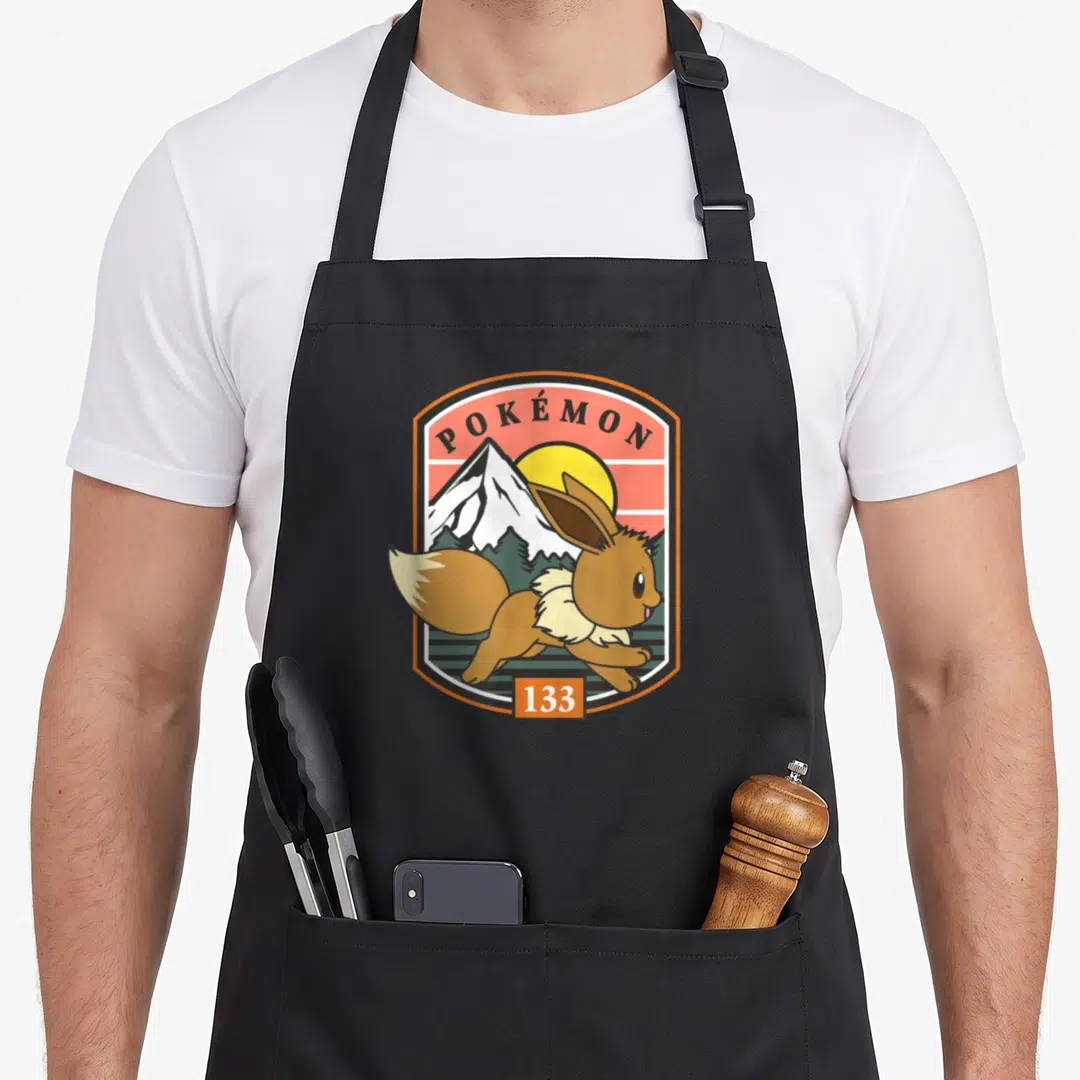 Pok outdoor apron - Eevee running in orange badge with POKÉMON 133 text and mountain sun background — shown on a black cotton canvas apron against a white background