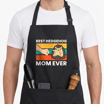 Vintage hedgehog mom apron - Fist bump between human hand and hedgehog on striped background with text — shown on a black cotton canvas apron against a white background
