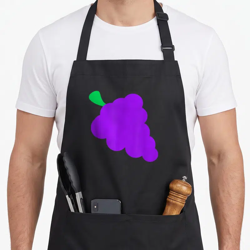 Funny grapes apron - Minimalist purple grape cluster with single green leaf on black bib — shown on a black cotton canvas apron against a white background