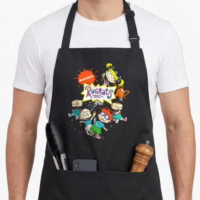 Cute portrait character aprons - Rugrats logo surrounded by cartoon babies in orange, yellow, blue, and purple — shown on a black cotton canvas apron against a white background