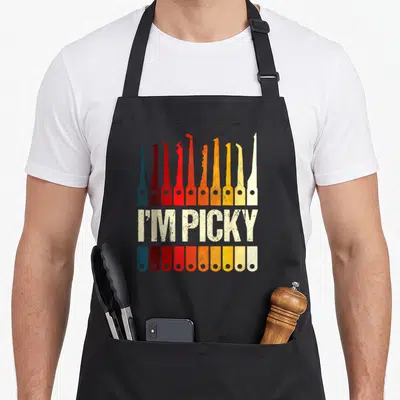 Locksmith picking apron - Ten colored lock picks and handles flanking distressed I'M PICKY text — shown on a black cotton canvas apron against a white background