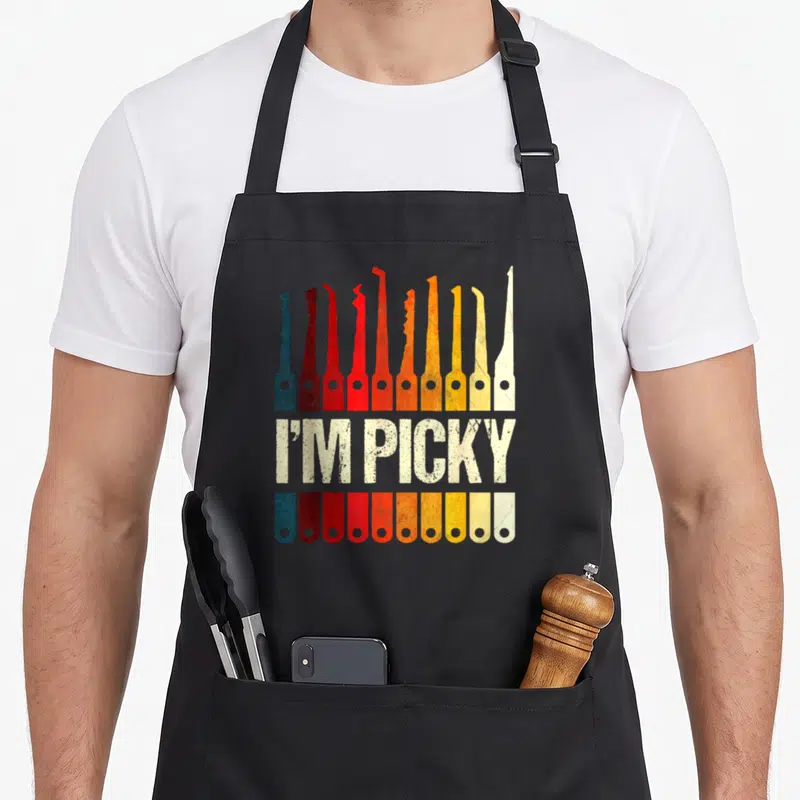 Locksmith picking apron - Ten colored lock picks and handles flanking distressed I'M PICKY text — shown on a black cotton canvas apron against a white background