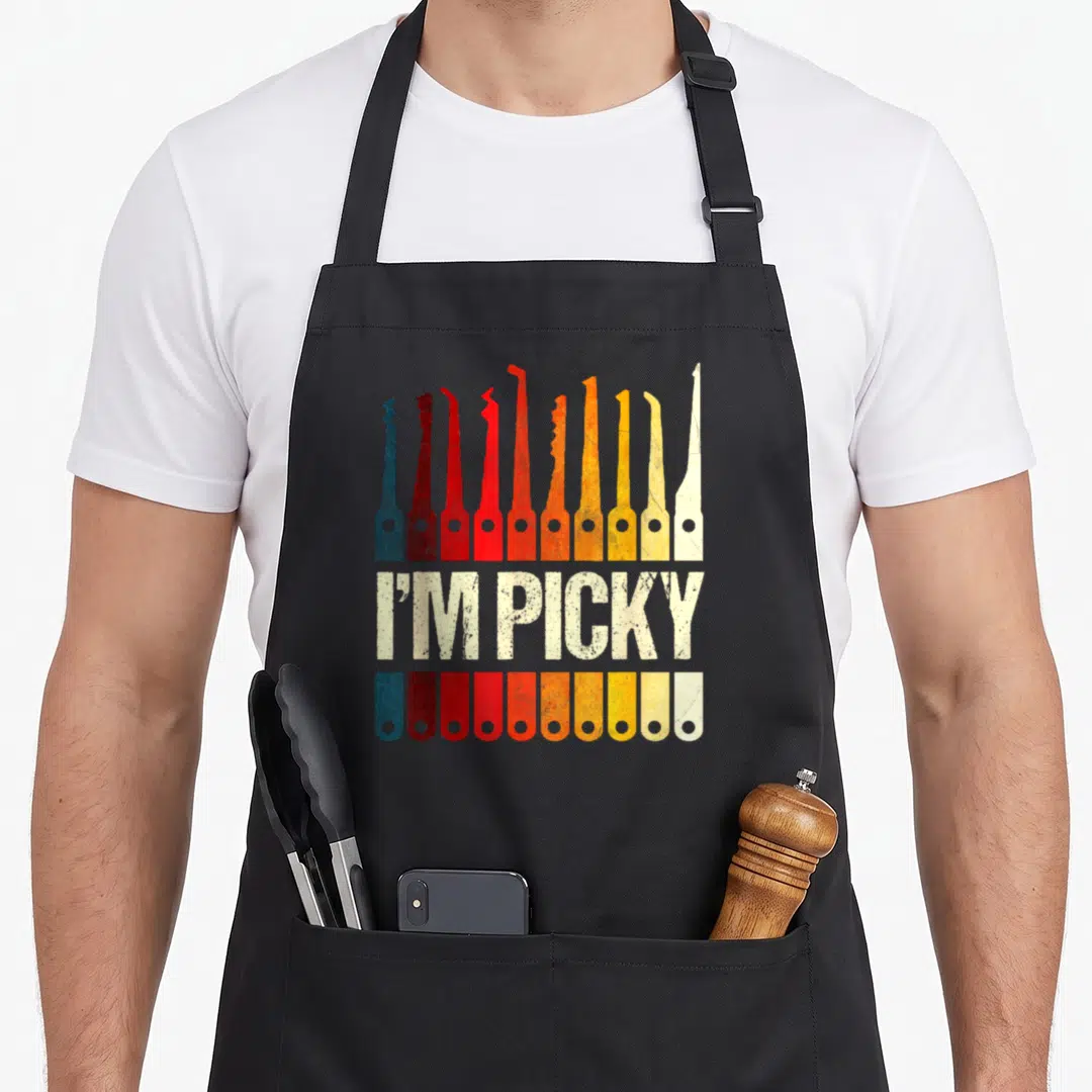 Locksmith picking apron - Ten colored lock picks and handles flanking distressed I'M PICKY text — shown on a black cotton canvas apron against a white background
