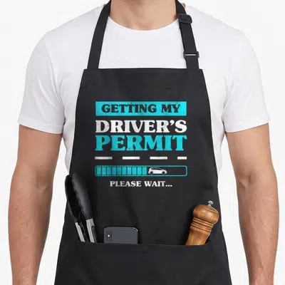 Permit congratulations apron - Stacked text Getting My Driver's Permit Please Wait loading bar car dashed lines — shown on a black cotton canvas apron against a white background