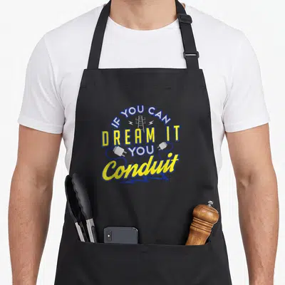 Pun electrician apron - Stacked IF YOU CAN DREAM IT YOU Conduit text with blue and yellow tower and plug graphics — shown on a black cotton canvas apron against a white background