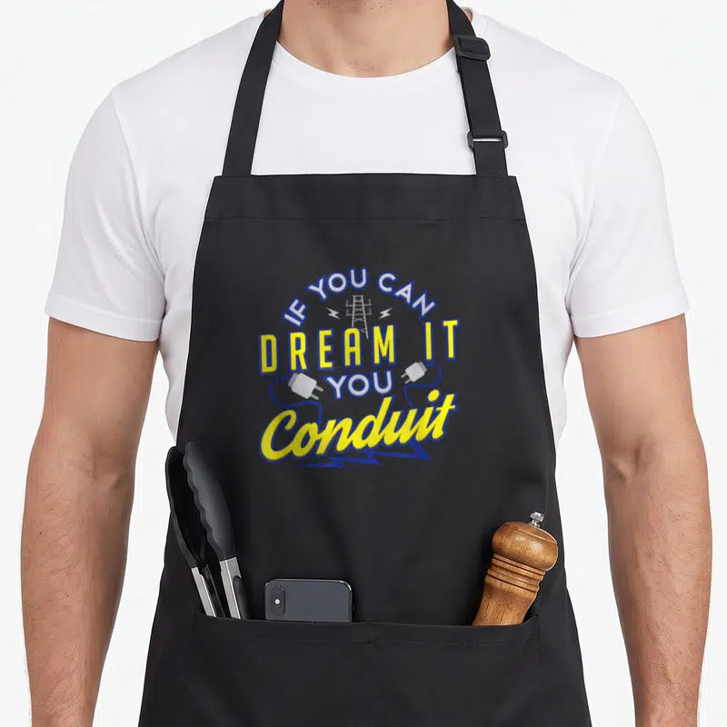 Pun electrician apron - Stacked IF YOU CAN DREAM IT YOU Conduit text with blue and yellow tower and plug graphics — shown on a black cotton canvas apron against a white background