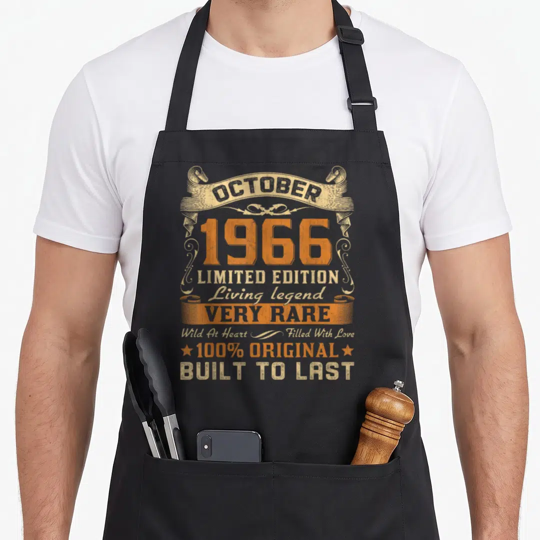 October bday birthday apron - Distressed orange and tan text reading October 1966 Limited Edition Living Legend Built — shown on a black cotton canvas apron against a white background