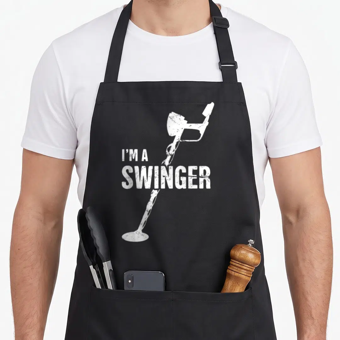 Swinger metal detecting apron - Distressed white I'M A SWINGER text over vertical metal detector illustration — shown on a black cotton canvas apron against a white background