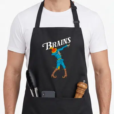 Dabbing wizard of oz apron - Arched BRAINS text above a leaning blue scarecrow zombie in cartoon style — shown on a black cotton canvas apron against a white background