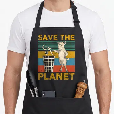 Hail goat apron - Cartoon goat throwing crescent cross and star into trash can under SAVE THE PLANET text on colored — shown on a black cotton canvas apron against a white background