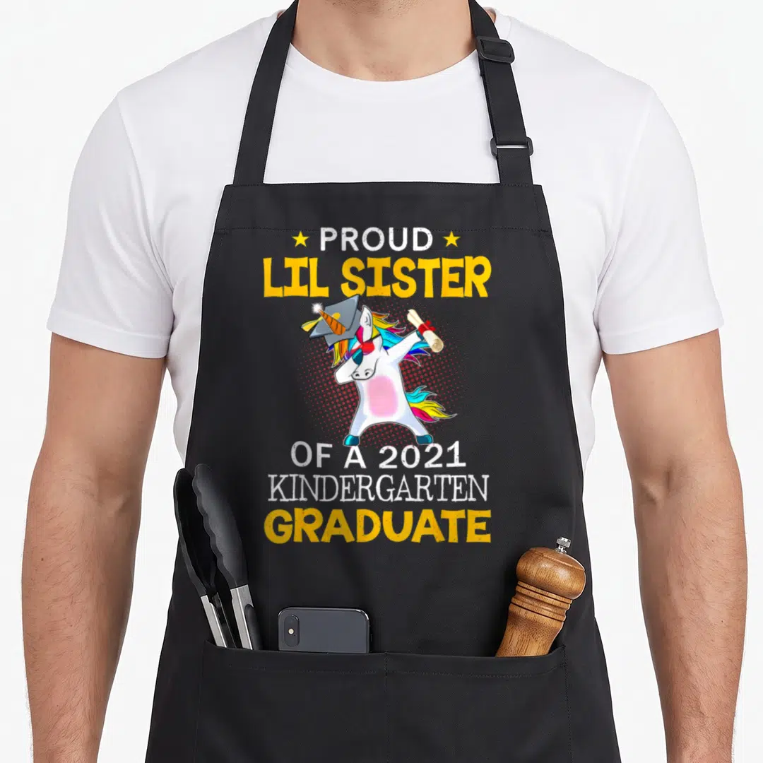 Lil unicorn aprons - Cartoon unicorn dabbing with diploma and cap surrounded by yellow and white text — shown on a black cotton canvas apron against a white background