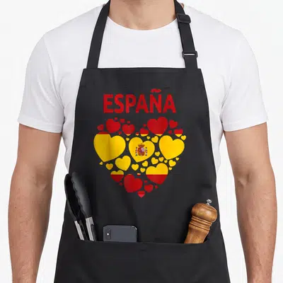 Spanish chef outfit with apron - ESPAÑA text above red and yellow heart collage with central coat of arms — shown on a black cotton canvas apron against a white background