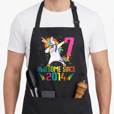 7th unicorn birthday apron - Dabbing unicorn with rainbow mane, pink number 7, and AWESOME SINCE 2014 text — shown on a black cotton canvas apron against a white background