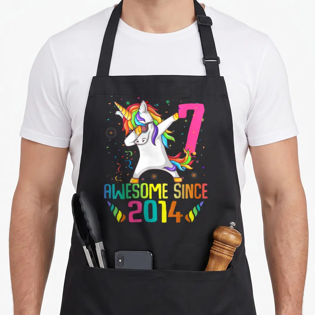 7th unicorn birthday apron - Dabbing unicorn with rainbow mane, pink number 7, and AWESOME SINCE 2014 text — shown on a black cotton canvas apron against a white background