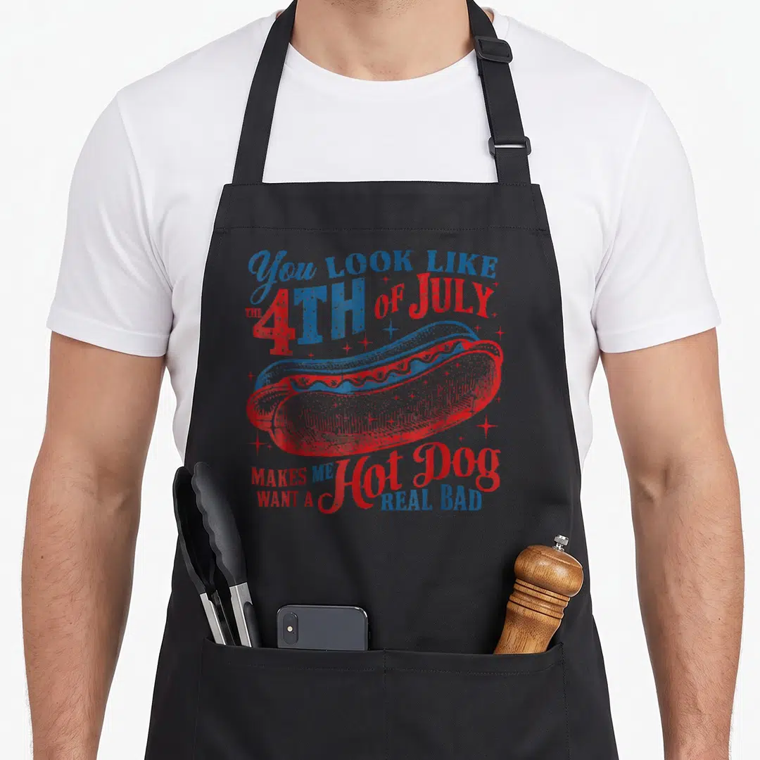 July hot dog apron - Patriotic hot dog illustration with distressed red blue white text and scattered stars — shown on a black cotton canvas apron against a white background