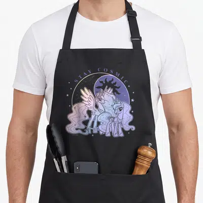 Stay magic apron - Two ponies under STAY COSMIC text with moon sun purple blue pink white — shown on a black cotton canvas apron against a white background