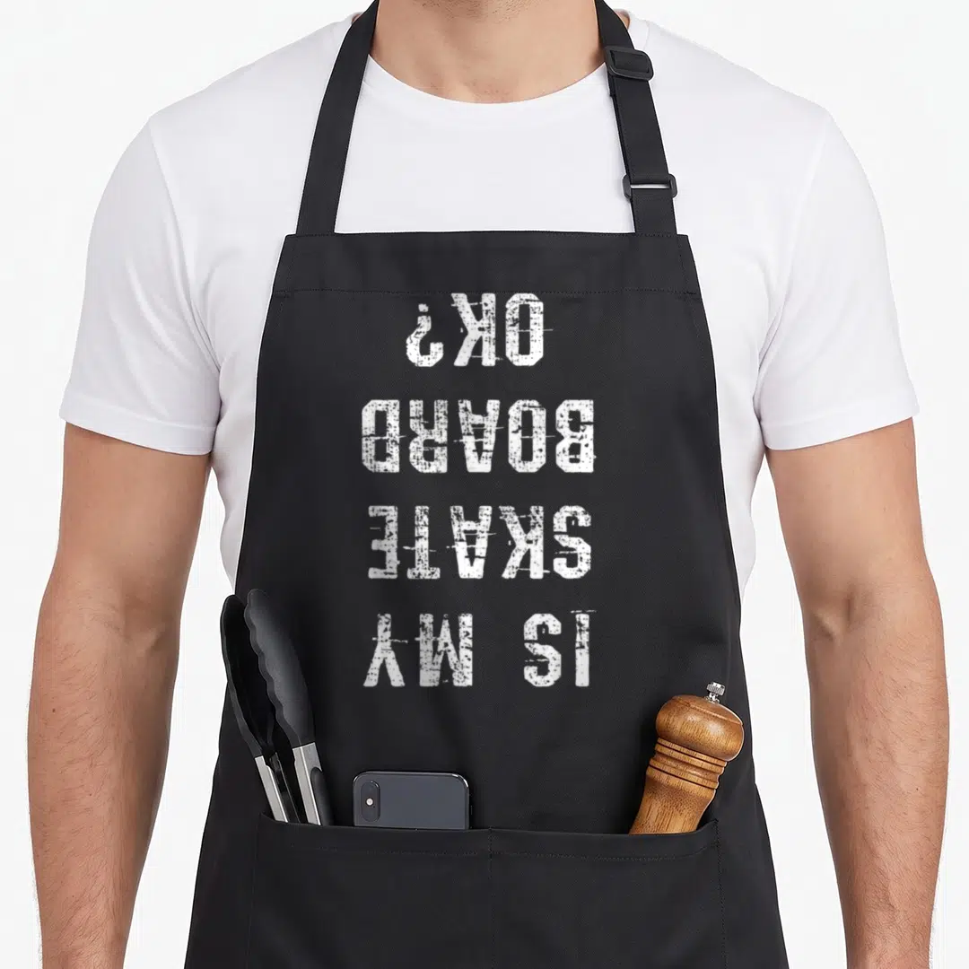 Skater skateboard funny apron - White stacked text reading IS MY SKATE BOARD OK? in inverted orientation — shown on a black cotton canvas apron against a white background