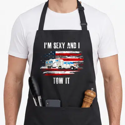 Flag camping apron - White truck towing camper on distressed red white blue flag with pun text — shown on a black cotton canvas apron against a white background