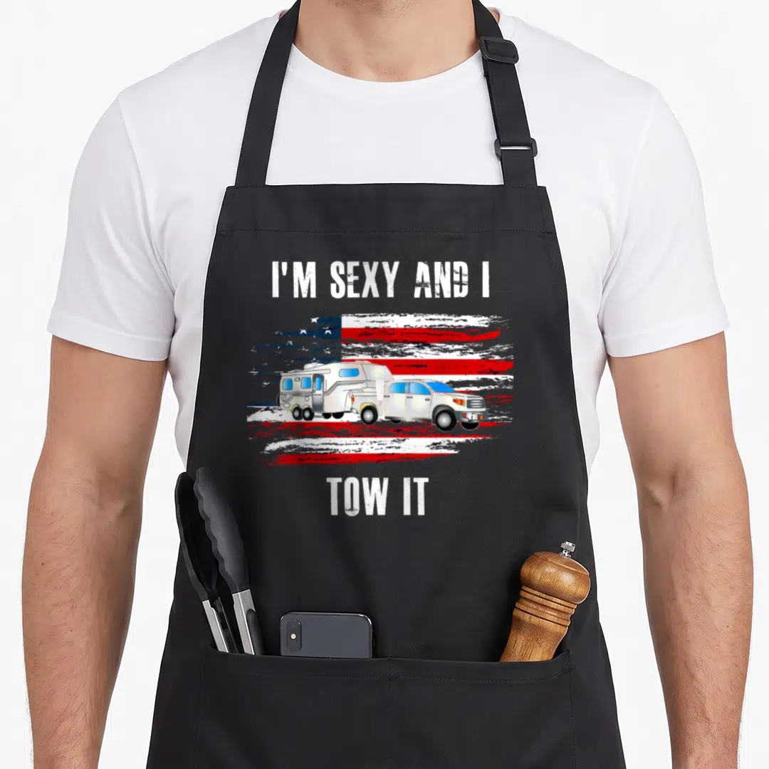Flag camping apron - White truck towing camper on distressed red white blue flag with pun text — shown on a black cotton canvas apron against a white background