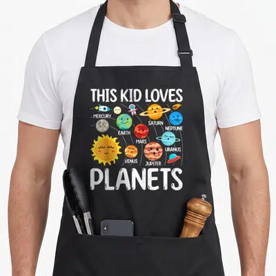 Star science apron - Cartoon solar system with labeled planets, rocket, astronaut, UFO, and white text reading THIS KID — shown on a black cotton canvas apron against a white background