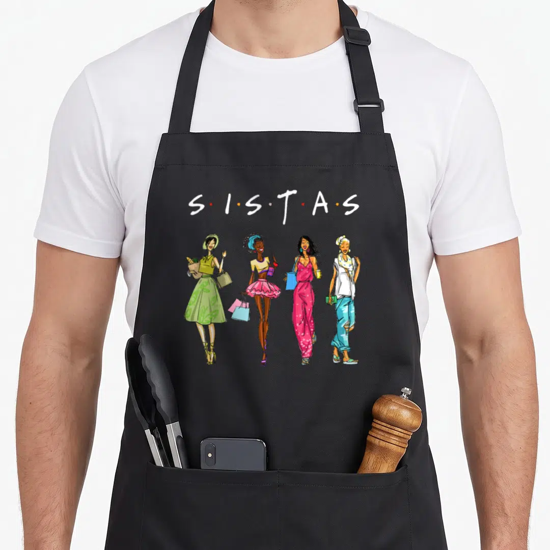 Sistas african print apron - Four cartoon women standing in a row below S.I.S.T.A.S text in pink, green, blue, yellow — shown on a black cotton canvas apron against a white background