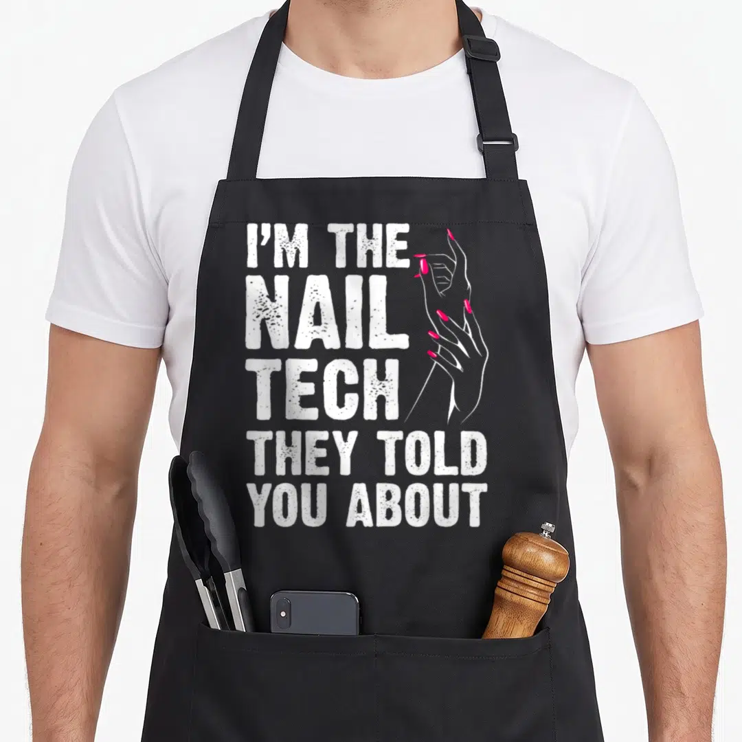 Nail tech manicurist apron - Distressed white text I'M THE NAIL TECH THEY TOLD YOU ABOUT beside two hands with pink — shown on a black cotton canvas apron against a white background