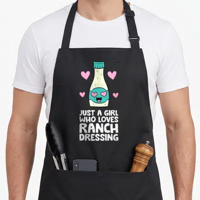 Cute ranch dressing apron - Cartoon ranch bottle with heart eyes and text Just A Girl Who Loves Ranch Dressing — shown on a black cotton canvas apron against a white background