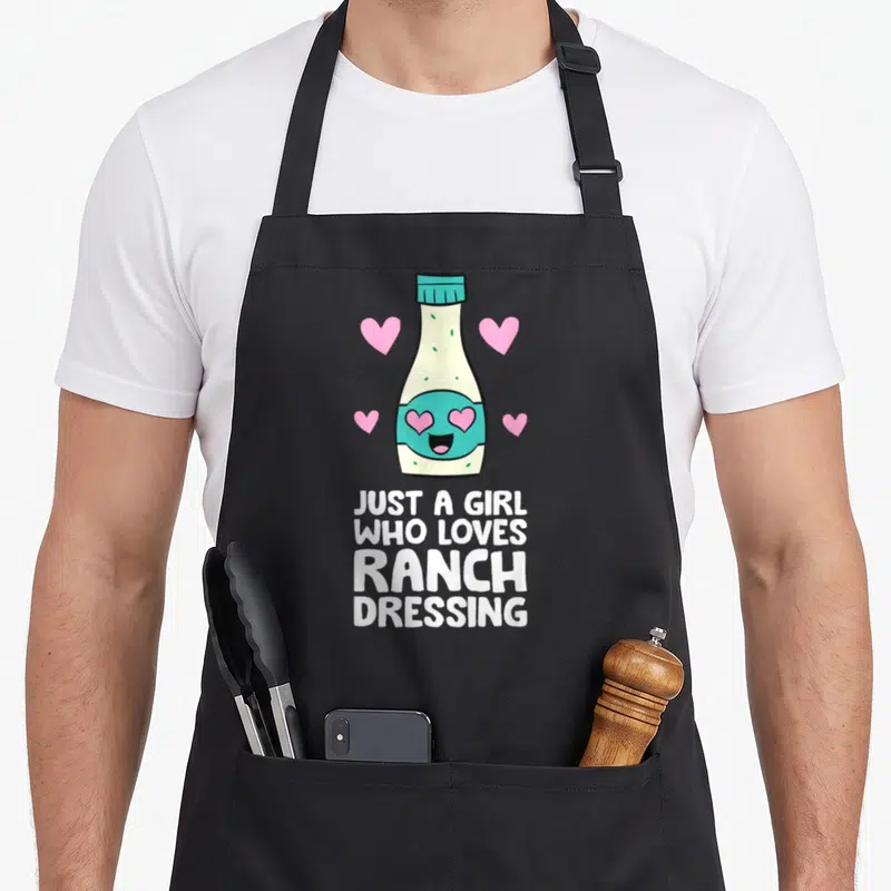 Cute ranch dressing apron - Cartoon ranch bottle with heart eyes and text Just A Girl Who Loves Ranch Dressing — shown on a black cotton canvas apron against a white background
