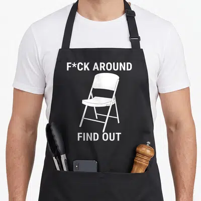 Around chair apron - White folding chair illustration between two lines of bold uppercase text reading F*CK AROUND FIND — shown on a black cotton canvas apron against a white background