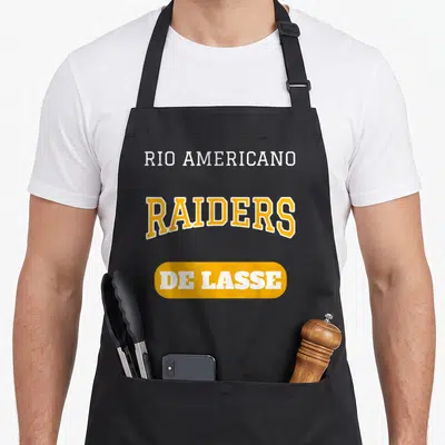 Rio teacher apron - Stacked yellow and white text reading Rio Americano Raiders De Lasse on black fabric — shown on a black cotton canvas apron against a white background