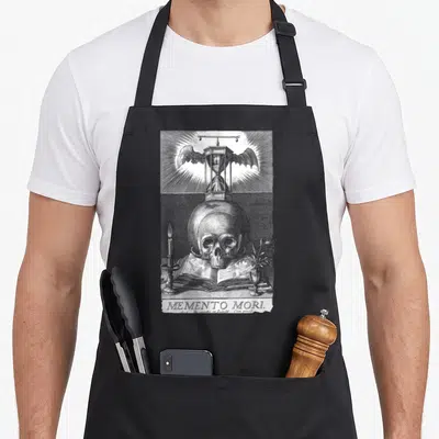 Memento philosopher apron - Grey line art skull on open book with winged hourglass and candle below MEMENTO MORI text — shown on a black cotton canvas apron against a white background