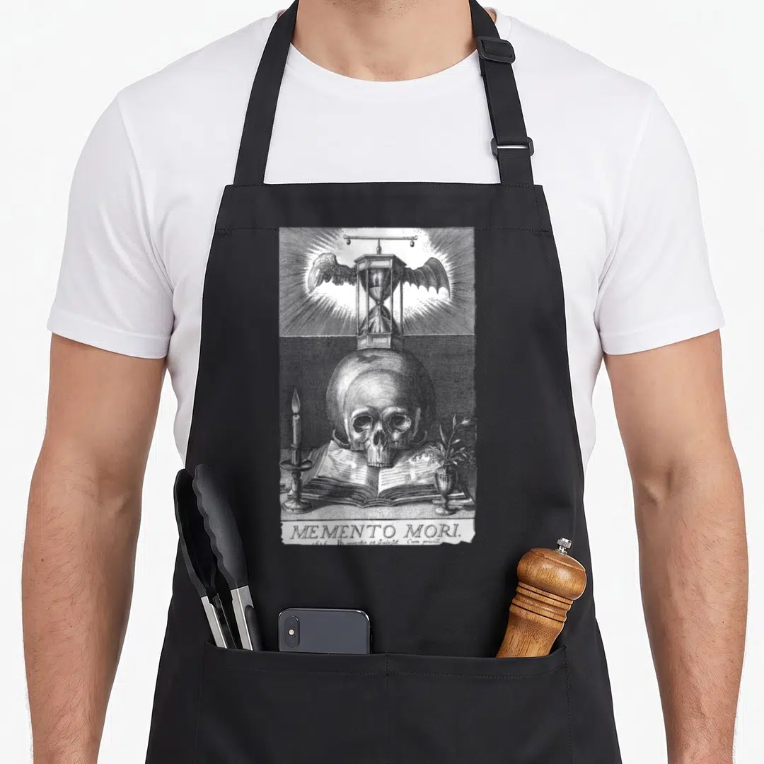 Memento philosopher apron - Grey line art skull on open book with winged hourglass and candle below MEMENTO MORI text — shown on a black cotton canvas apron against a white background