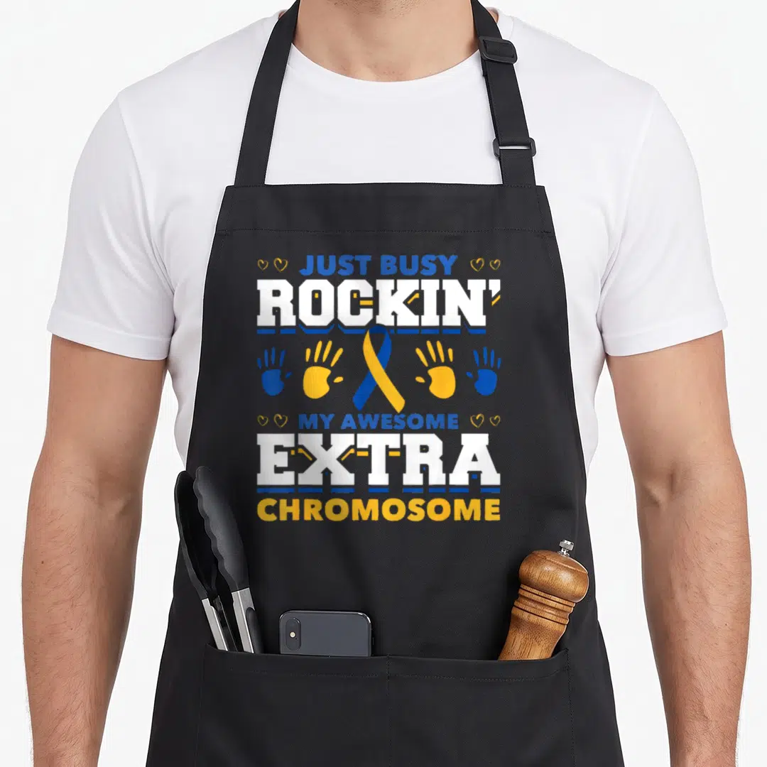 Rockin busy apron - Just Busy Rockin My Awesome Extra Chromosome text with blue yellow ribbon and handprints — shown on a black cotton canvas apron against a white background