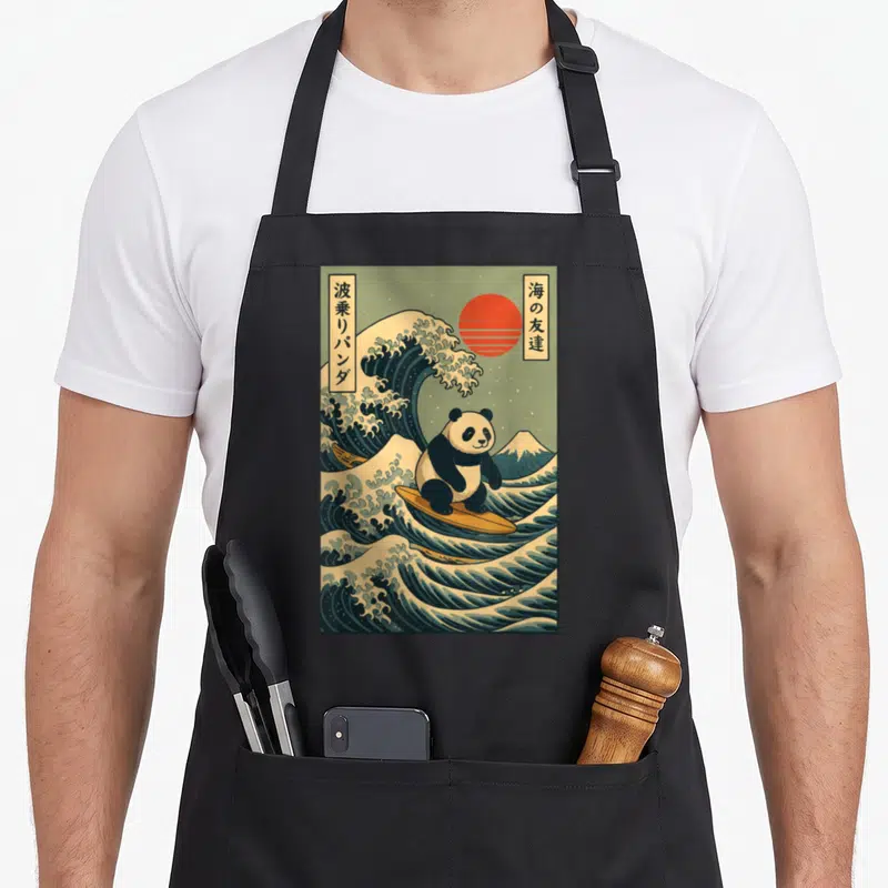 Panda surfing apron - Retro panda surfing on blue waves with red sun and Japanese text boxes — shown on a black cotton canvas apron against a white background