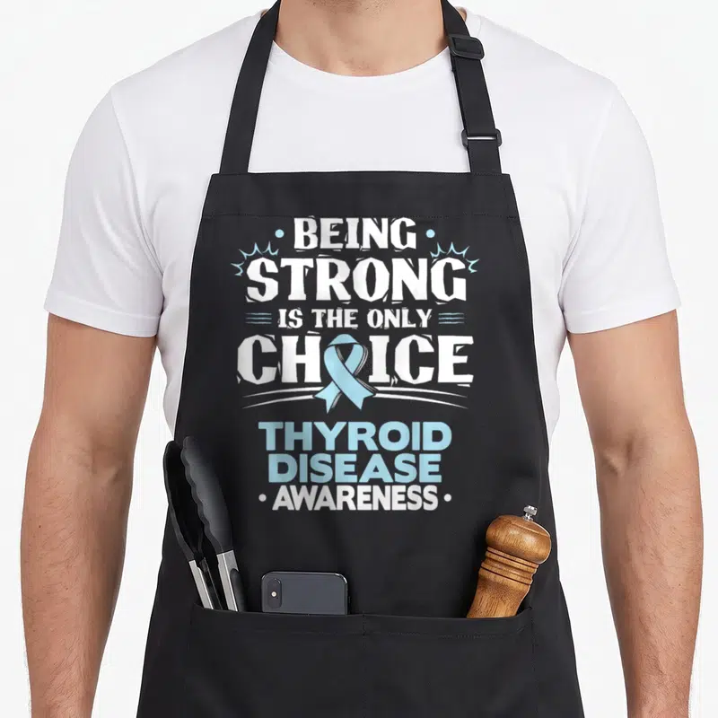 Disease thyroid apron - White and blue text reading being strong is the only choice with light blue ribbon overlapping — shown on a black cotton canvas apron against a white background