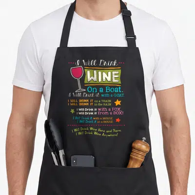 Drink wine apron - Stacked text listing wine drinking locations with a wine glass icon and scattered stars — shown on a black cotton canvas apron against a white background