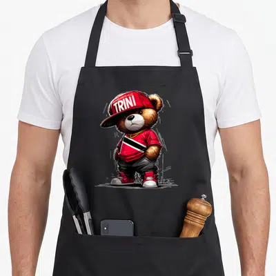 Unapologetically teddy bear apron - Cartoon bear in red cap with UNAPOLOGETICALLY TRINI text and striped shirt — shown on a black cotton canvas apron against a white background