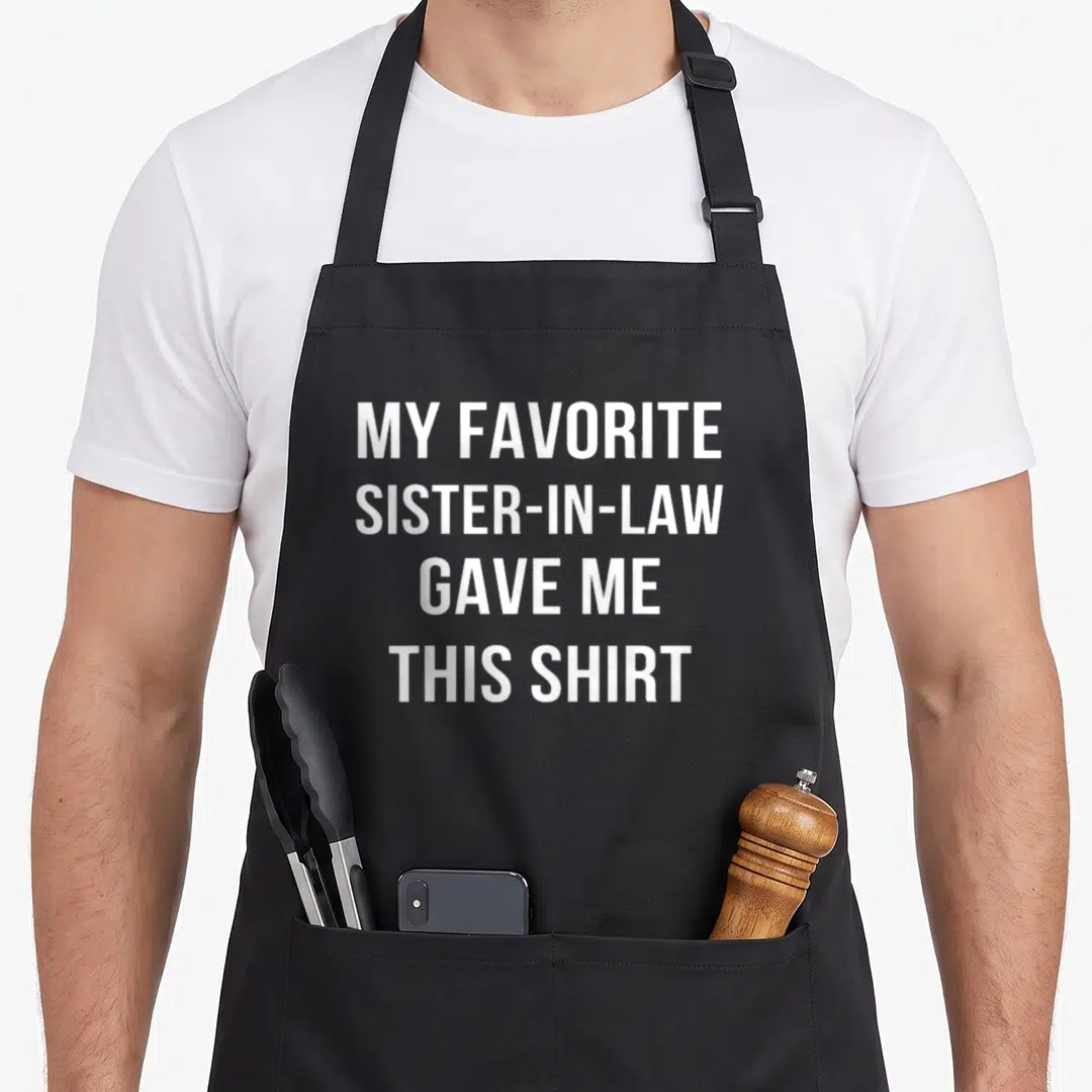 Sister birthday apron - White text reading My Favorite Sister-In-Law Gave Me This Shirt — shown on a black cotton canvas apron against a white background