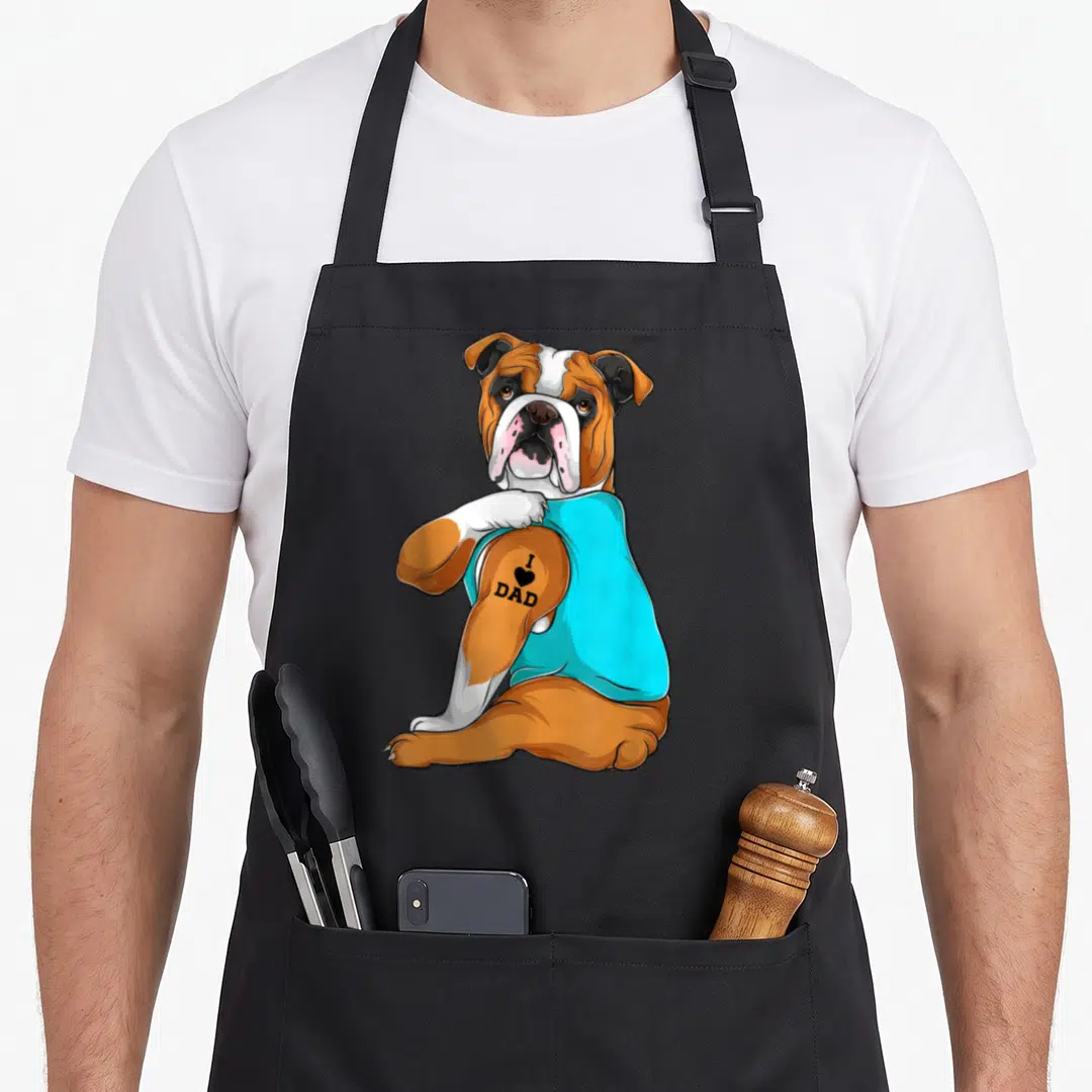 English tattoo aprons - Cartoon bulldog in cyan shirt with I Love Dad tattoo on brown arm — shown on a black cotton canvas apron against a white background