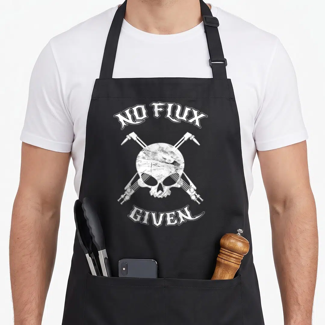 Flux welder dad apron - Distressed white skull with crossed soldering irons and arched text on black fabric — shown on a black cotton canvas apron against a white background