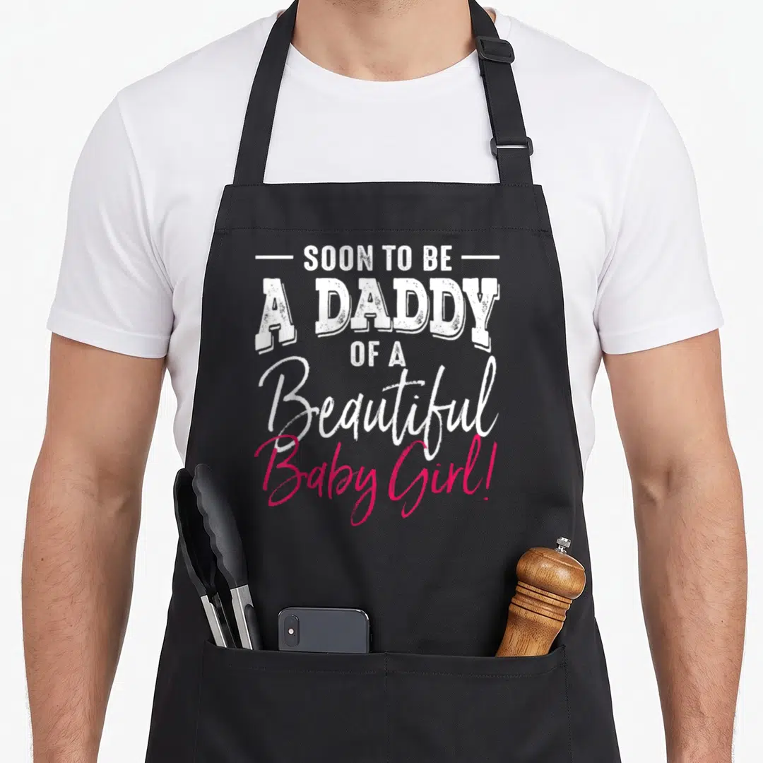 Expecting daddy apron - White and pink typography reading Soon To Be A Daddy Of A Beautiful Baby Girl — shown on a black cotton canvas apron against a white background