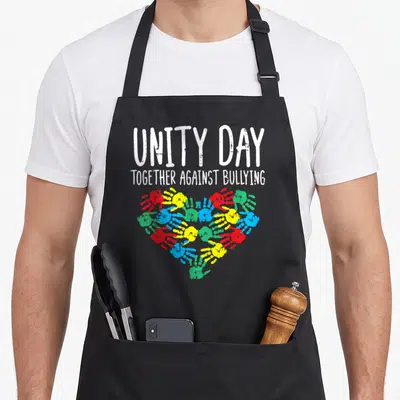 Together against unity day apron - White text UNITY DAY TOGETHER AGAINST BULLYING above red yellow green blue handprint — shown on a black cotton canvas apron against a white background