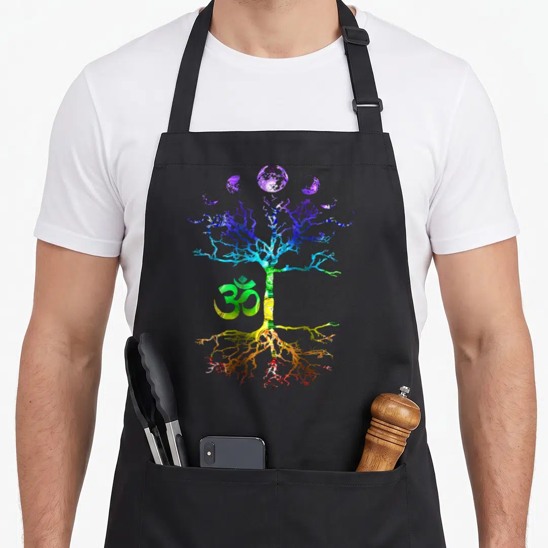 Phase tree apron - Rainbow tree with Om, moon phases, and chakra symbols in cartoon style — shown on a black cotton canvas apron against a white background