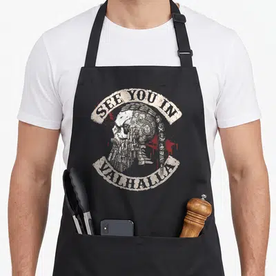 See valhalla viking apron - Distressed skull with braided beard and SEE YOU IN VALHALLA text on black apron — shown on a black cotton canvas apron against a white background