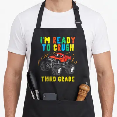 Crush 3rd truck apron - Red monster truck with colorful text I'm ready to crush third grade — shown on a black cotton canvas apron against a white background